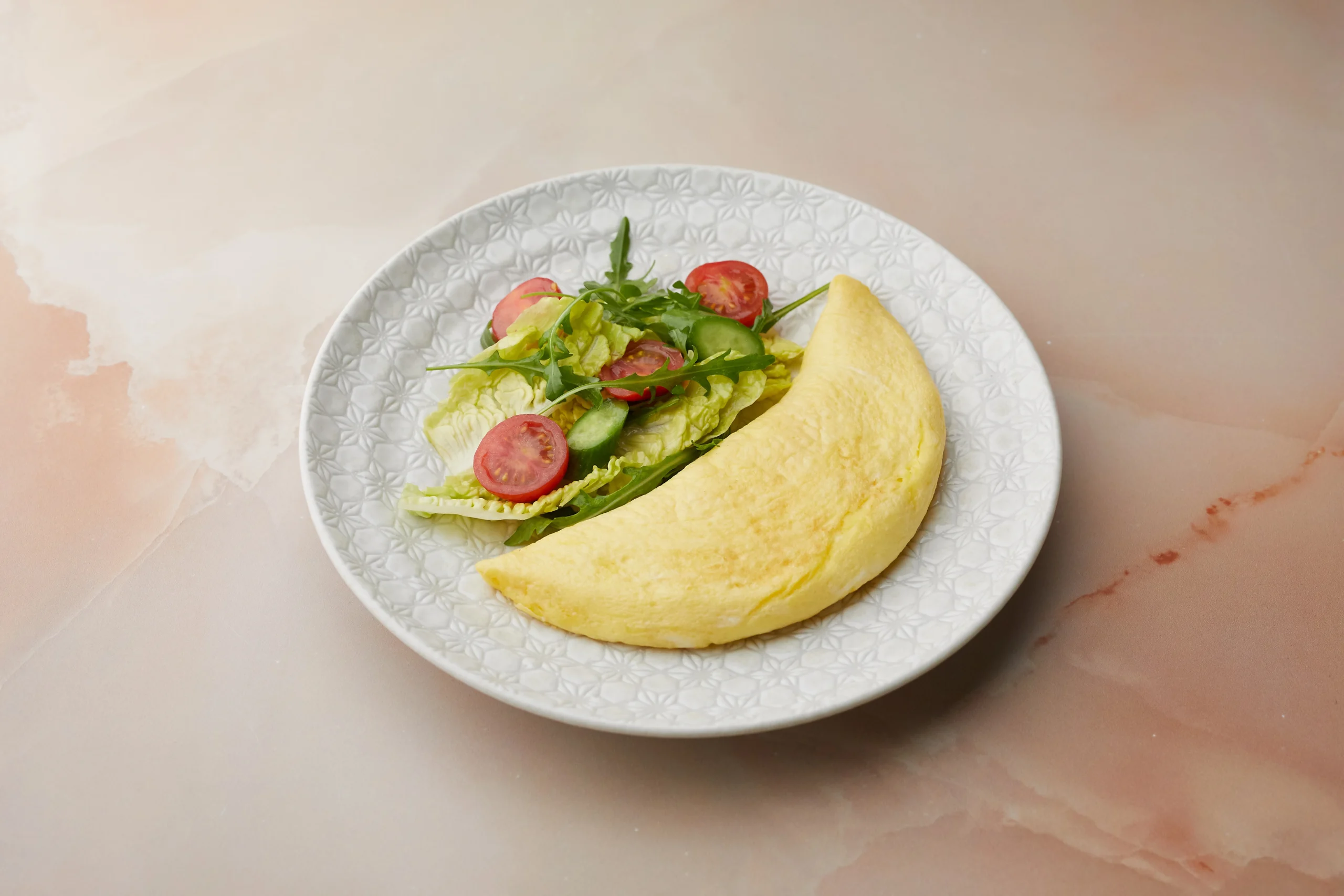 Fluffy folded omelette served with a fresh side salad of lettuce, cherry tomatoes, cucumber, and arugula on a patterned white plate at MYA, Dubai Mall.