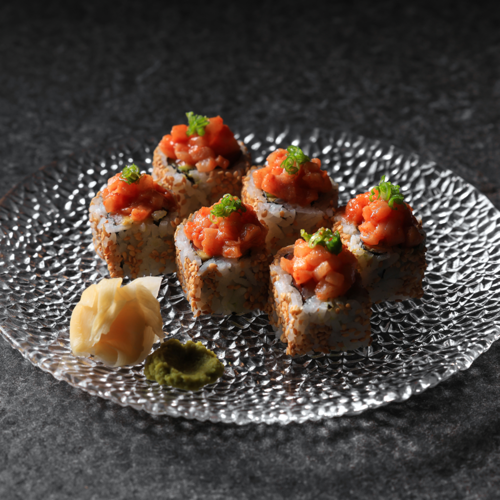 Spicy salmon sushi rolls topped with diced salmon and green onion on a textured glass plate.
