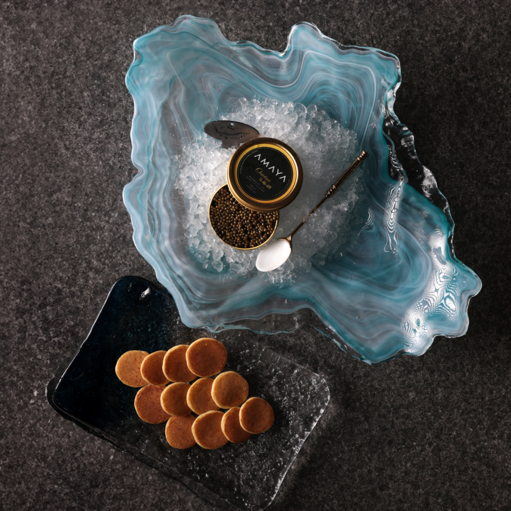 Premium caviar served on ice with blinis and a pearl spoon in a blue decorative bowl.