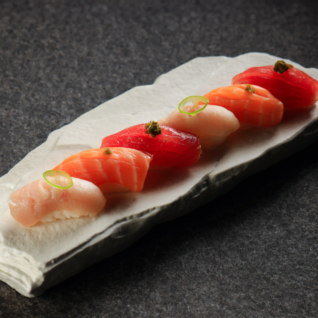 Assorted premium nigiri sushi with salmon and white fish, elegantly plated on a ceramic serving dish with delicate garnish.